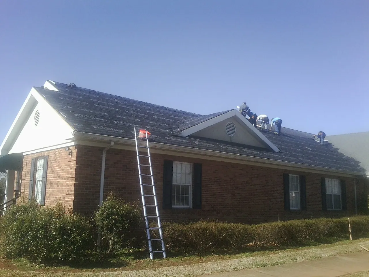 Crew tearing shingles off a brick ranch roof with a ladder set — Emergency Roof Repair work by our crew in Polk
