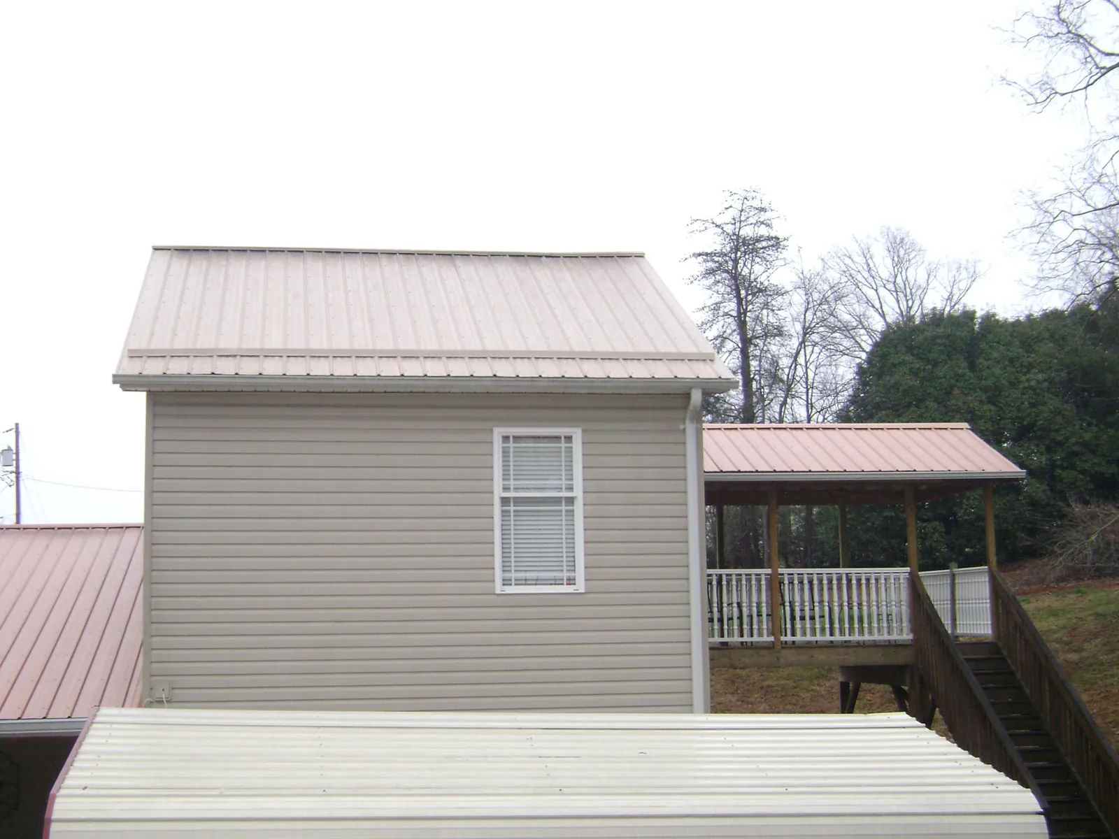 Tan metal roofs on a two story addition and attached porch, from a Roof Replacement job in Polk